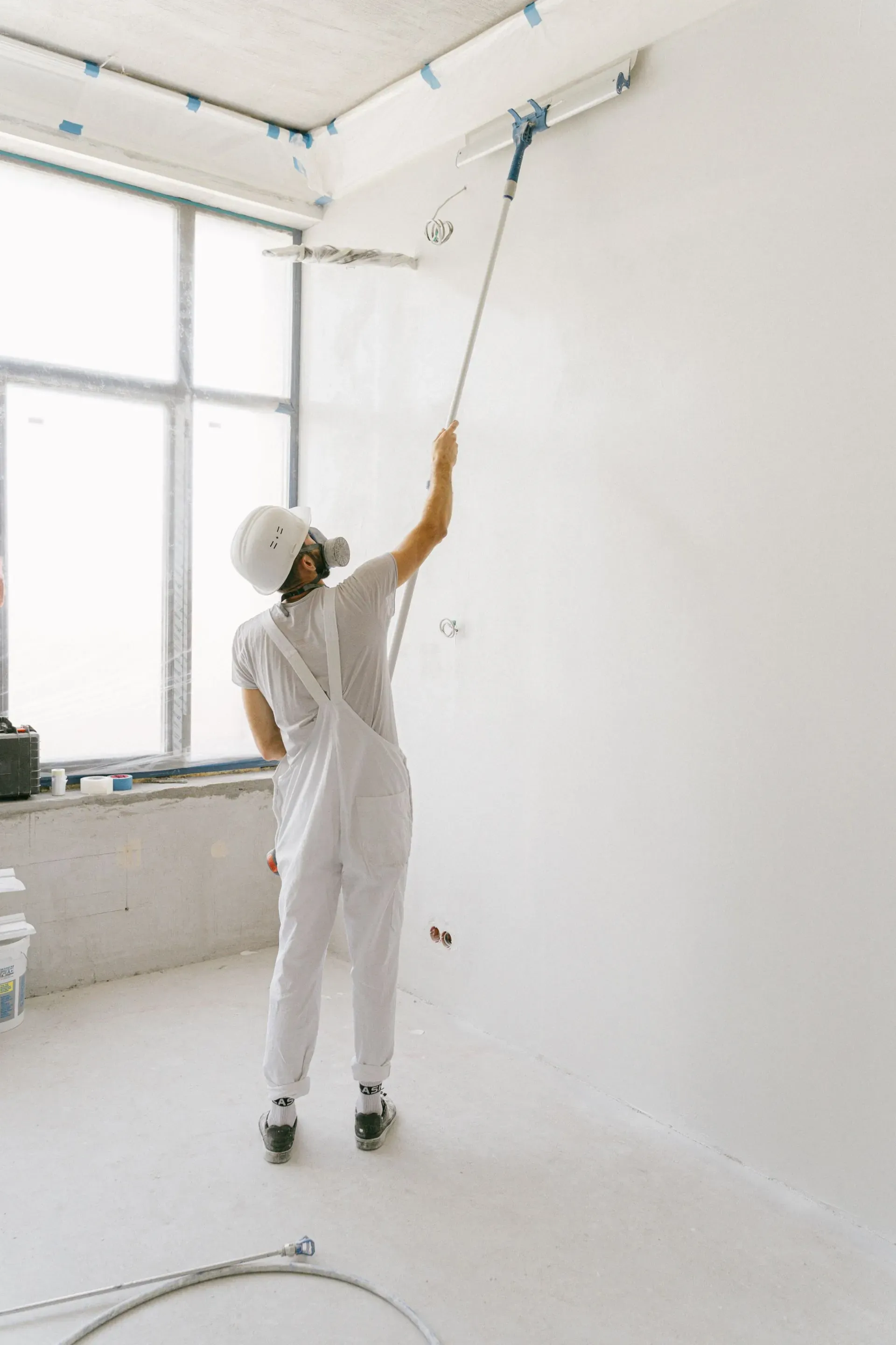 Worker in white protective clothing restoring a bright empty room.