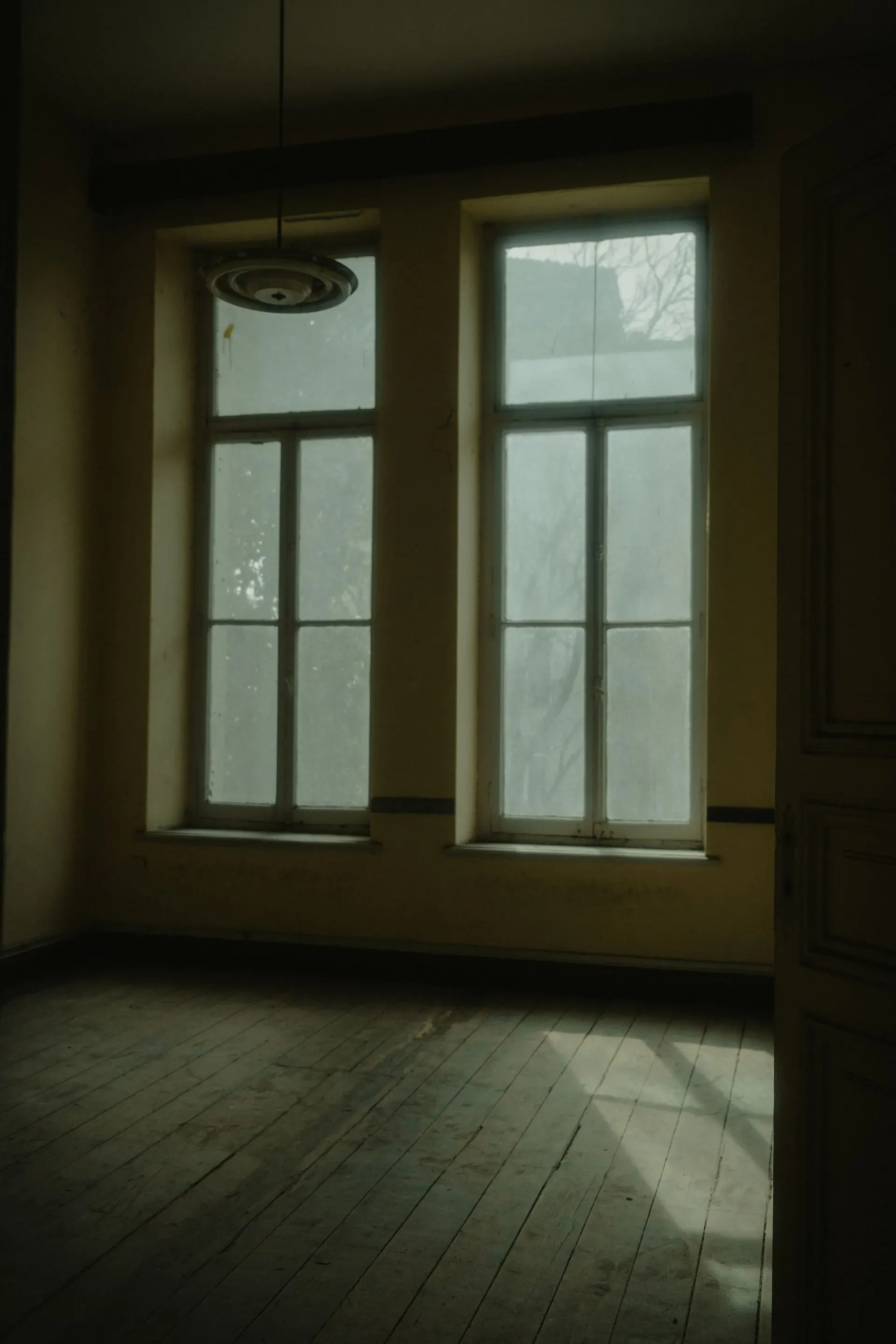 Dim empty room with tall windows and shadowed green-toned floor.