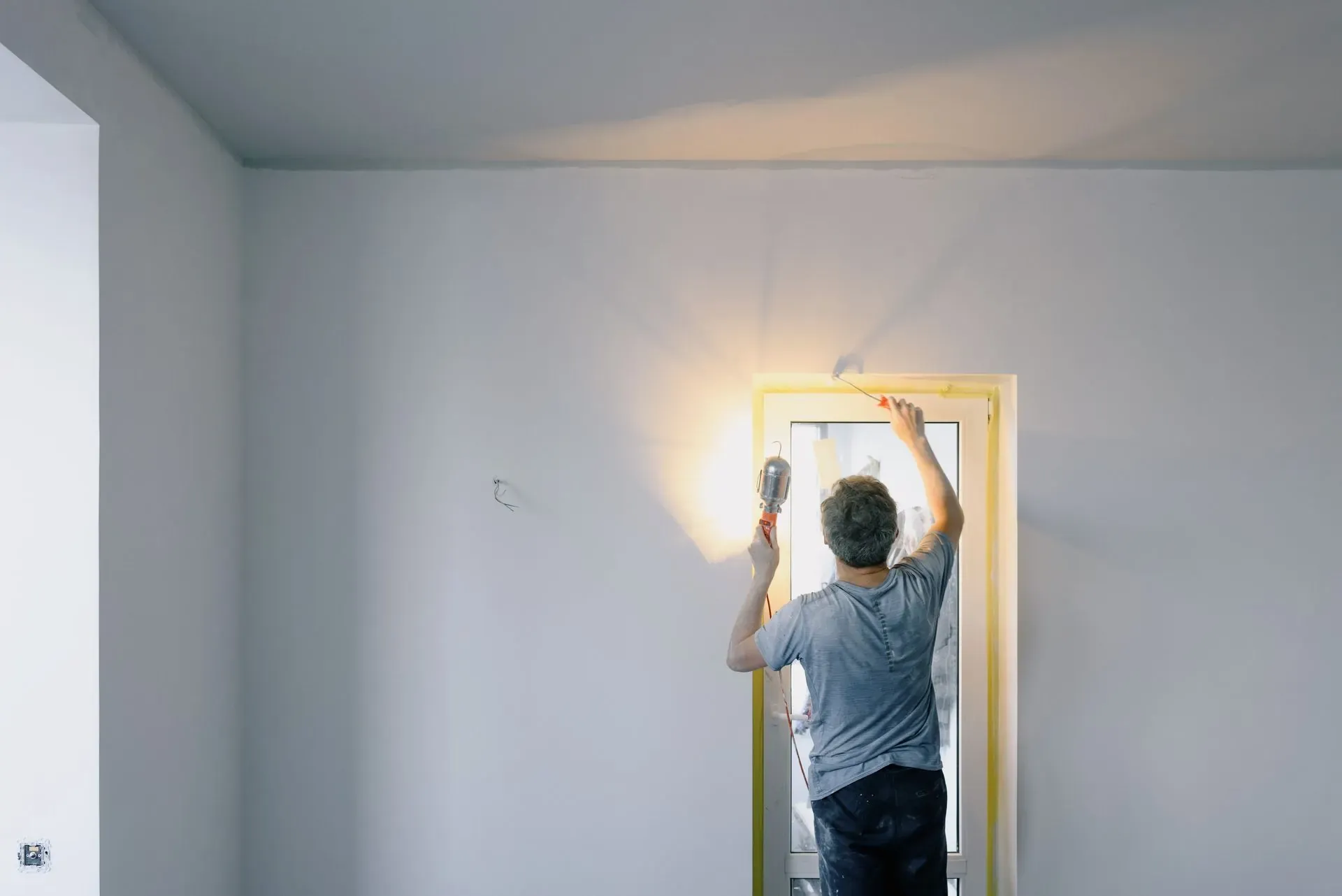 Worker finishing a doorway in a clean white room after renovation.