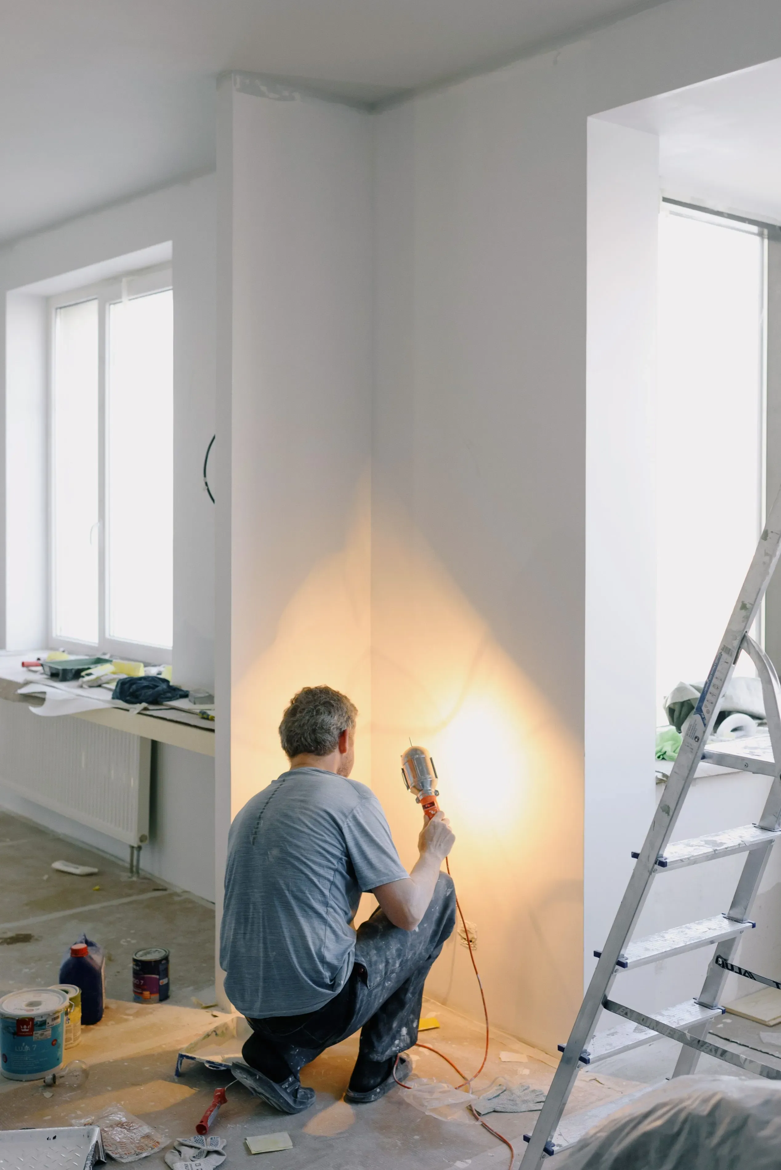 Technician kneeling with a work light in a bright room under renovation.