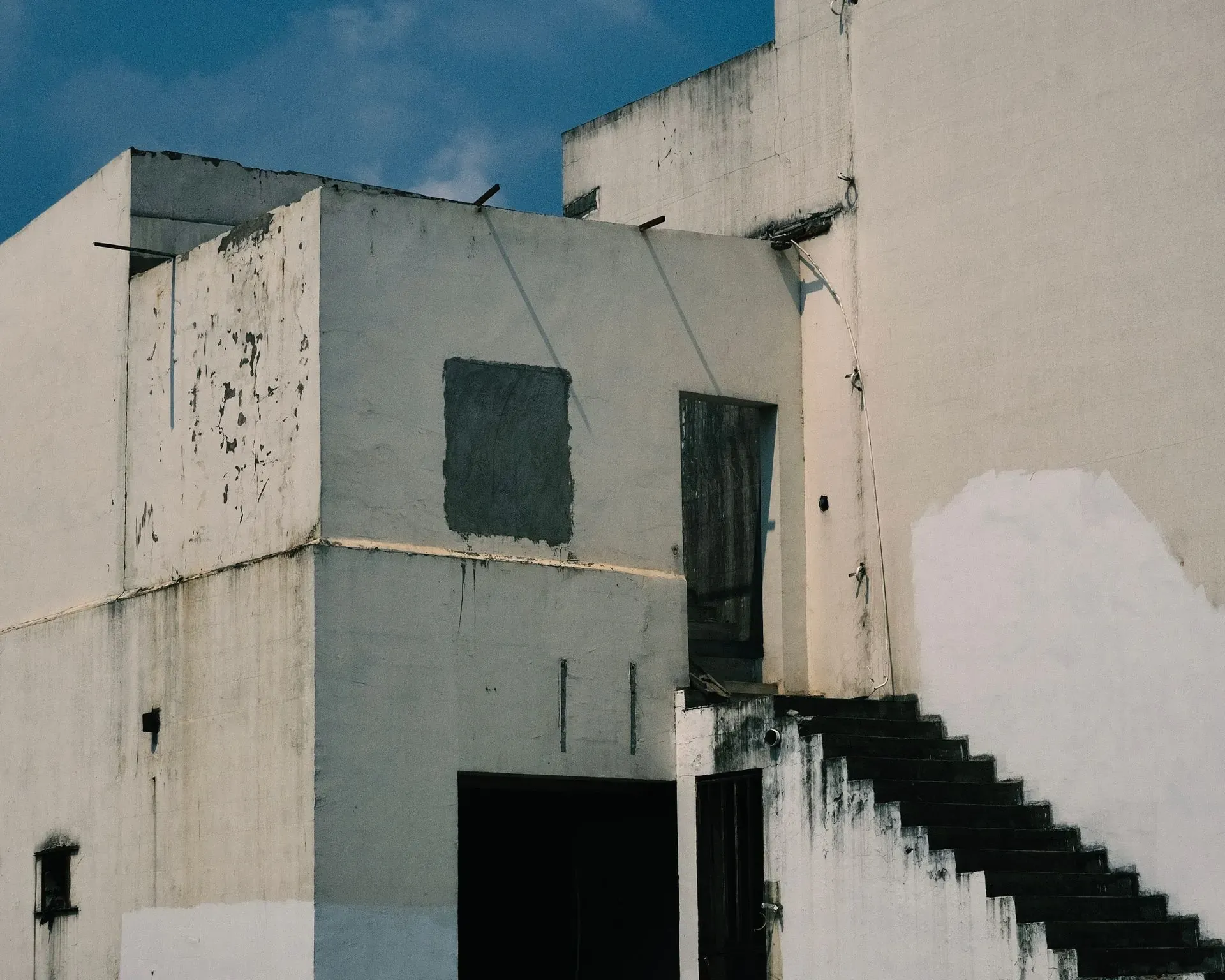 Weathered white exterior wall with dark mildew-like staining near stairs.